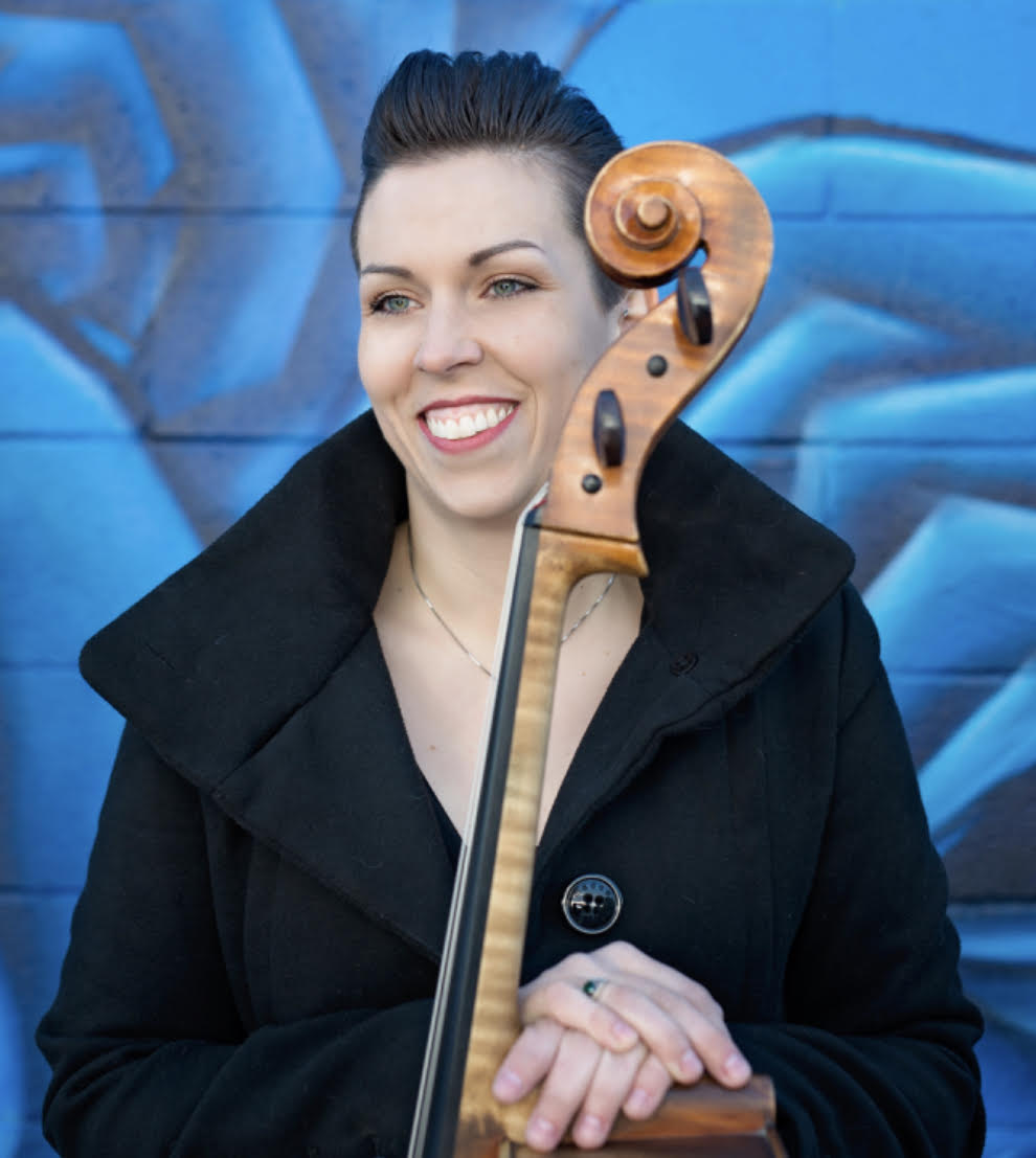 A woman in a black coat smiling with a cello in her hands