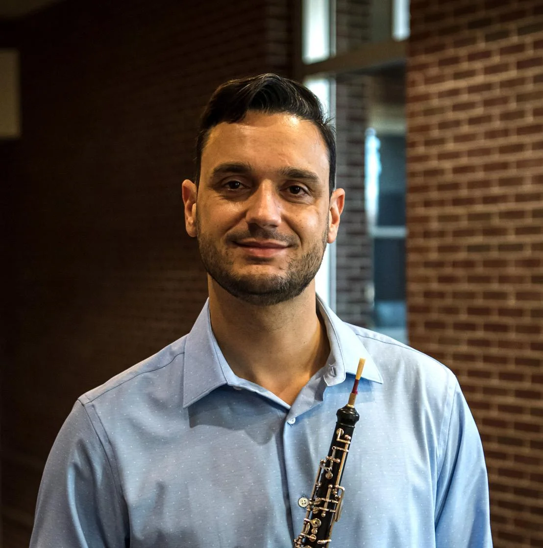 A man holding an oboe and standing in front of a brick wall